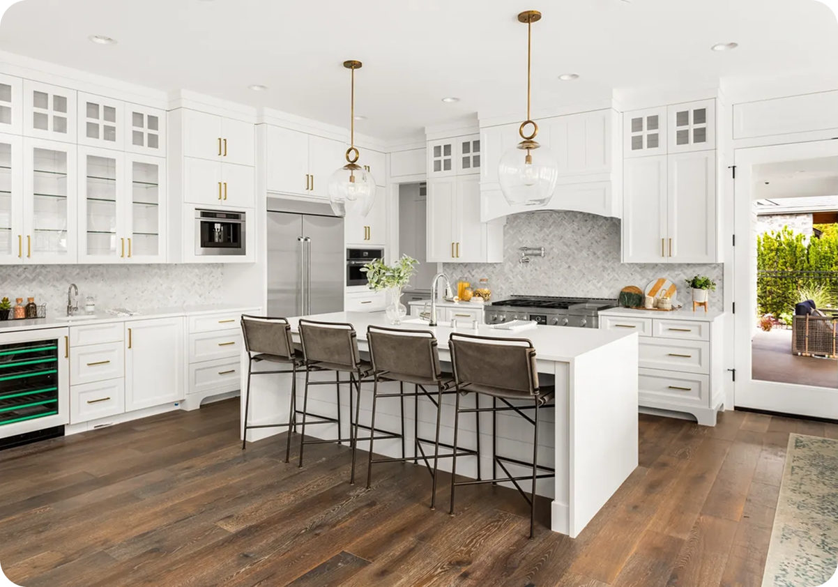 Spacious modern kitchen with white cabinets, central island with four chairs, pendant lights, stainless steel appliances, and wooden flooring.